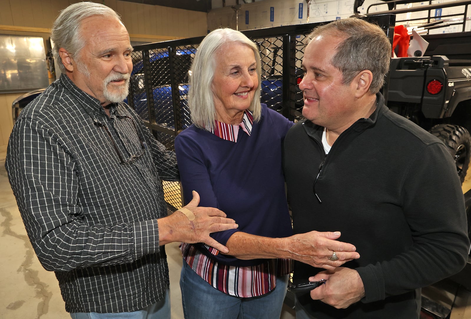 Patrick Driscoll gets a hug by Timothy and Joyce Seymour Friday, April 15, 2022 in his hanger at Andy Barnhart Memorial Airport in New Carlisle. Driscoll is receiving the Carnegie Medal for Civilian Heroism for risking his life to save the Seymours from their burning plane after it crashed at the airport. BILL LACKEY/STAFF