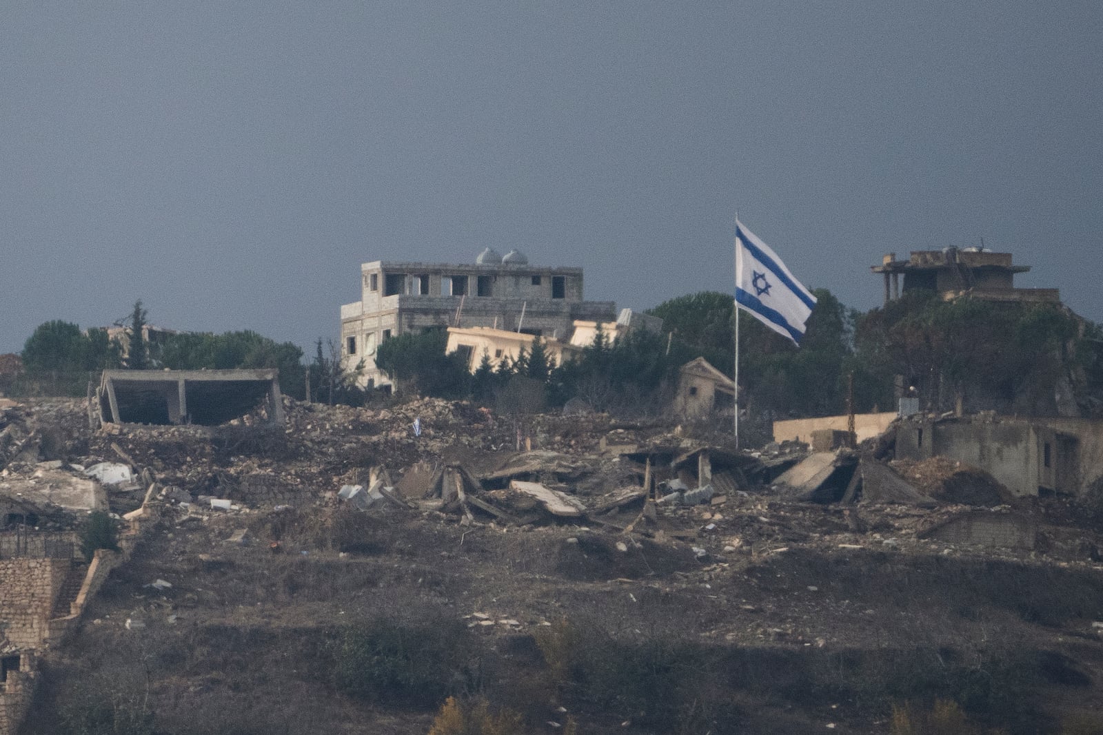 An Israeli flag stands next to damaged buildings on an area in southern Lebanon as seen from northern Israel, Tuesday, Nov. 19, 2024. (AP Photo/Leo Correa)