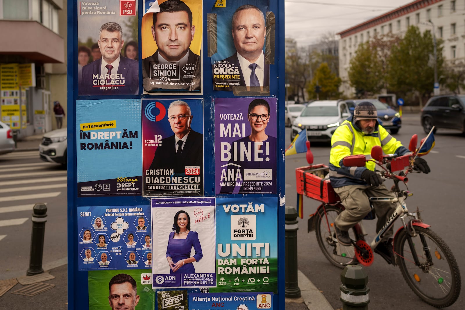 A man rides a bicycle passing panels displaying electoral posters ahead of the Nov. 24 presidential elections in Bucharest, Romania, Friday, Nov. 22, 2024. (AP Photo/Vadim Ghirda)