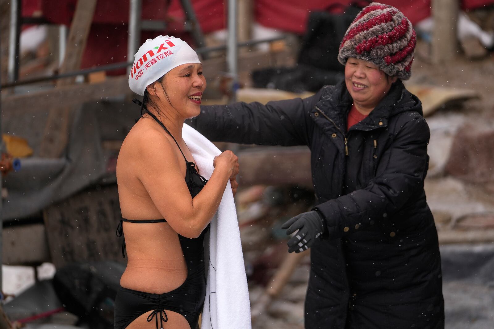 A woman passes a towel to a swimmer after she swims in a pool carved from ice on the frozen Songhua river in Harbin in northeastern China's Heilongjiang province, Tuesday, Jan. 7, 2025. (AP Photo/Andy Wong)