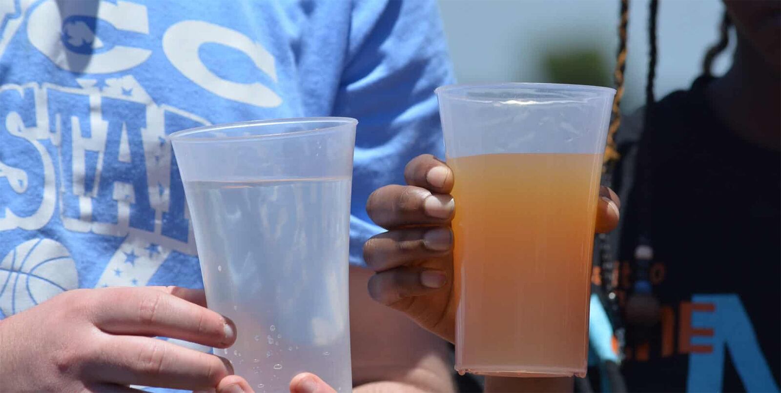 Spring Valley Academy students  Devaney Ross (L) and Justin Bekowies are shown holding dirty water from a poluted water source in Kenya and clean water after it has been filtered.