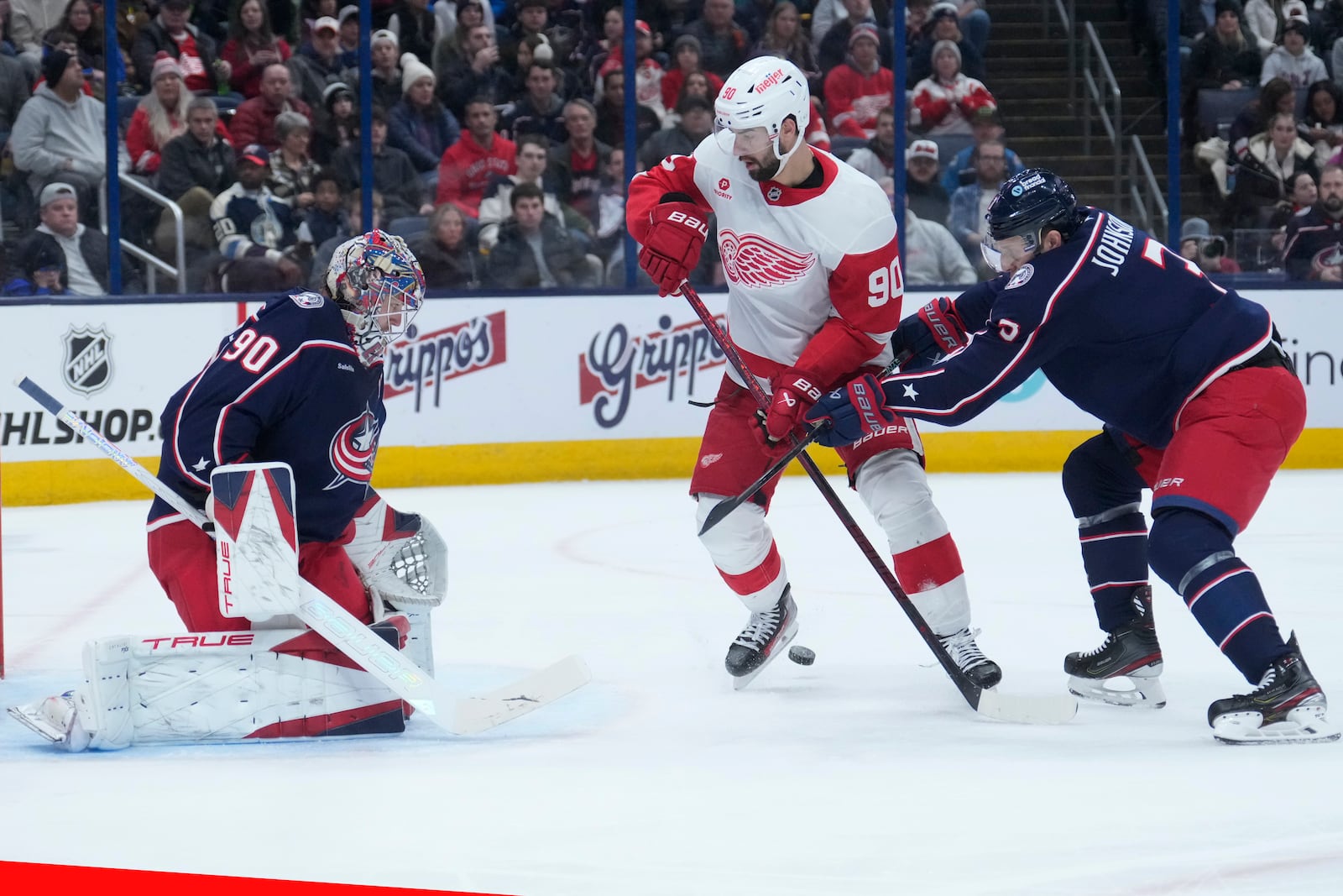 Columbus Blue Jackets defenseman Jack Johnson (3) defends Detroit Red Wings center Joe Veleno, right, in front of goaltender Elvis Merzlikins, left, in the first period of an NHL hockey game in Columbus, Ohio, Thursday, Jan. 2, 2025. (AP Photo/Sue Ogrocki)