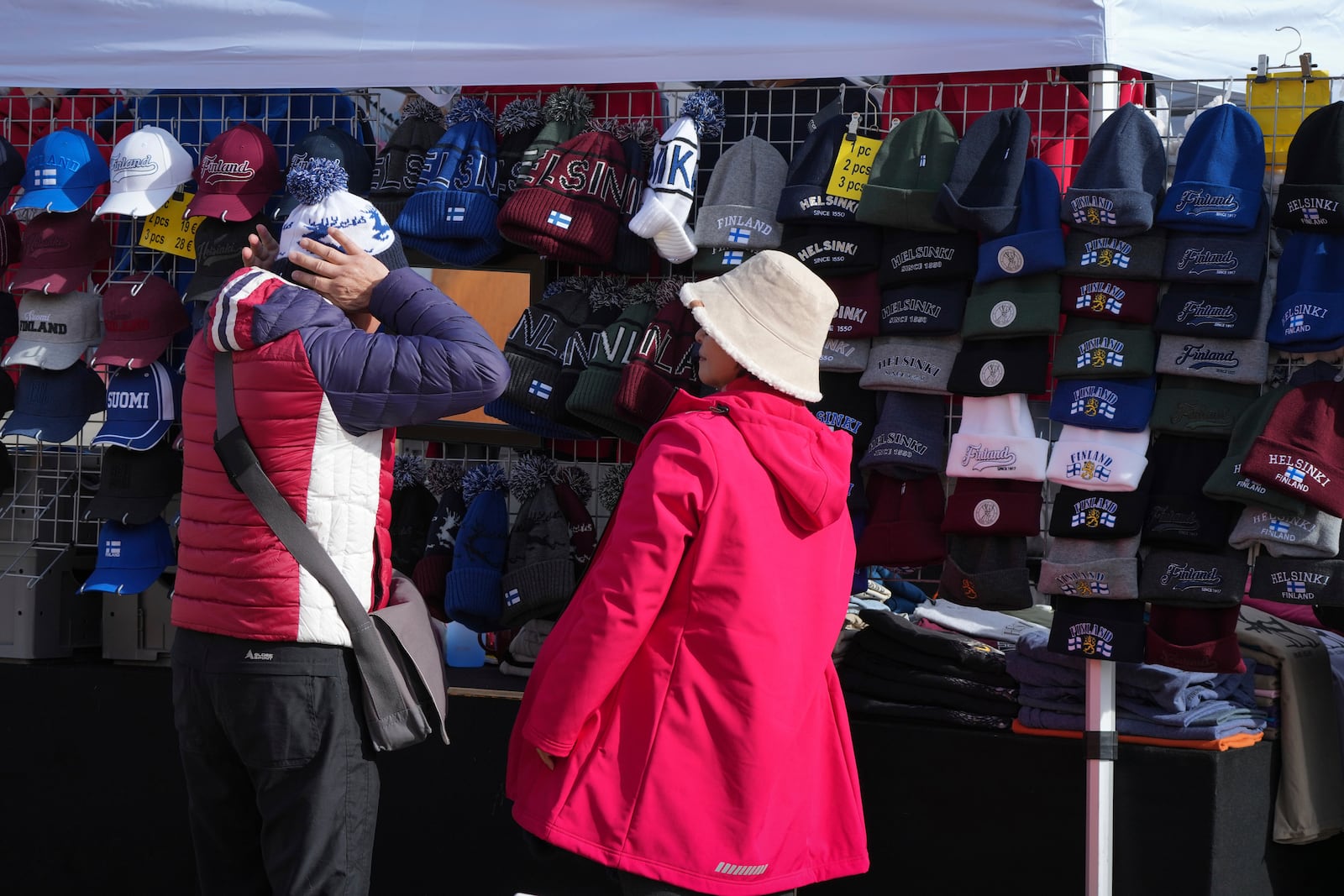 A man trying on a knitted hat with Finnish pattern on the Market Square in the center of Helsinki, Finland, Saturday, March 15, 2025. (AP Photo/Sergei Grits)