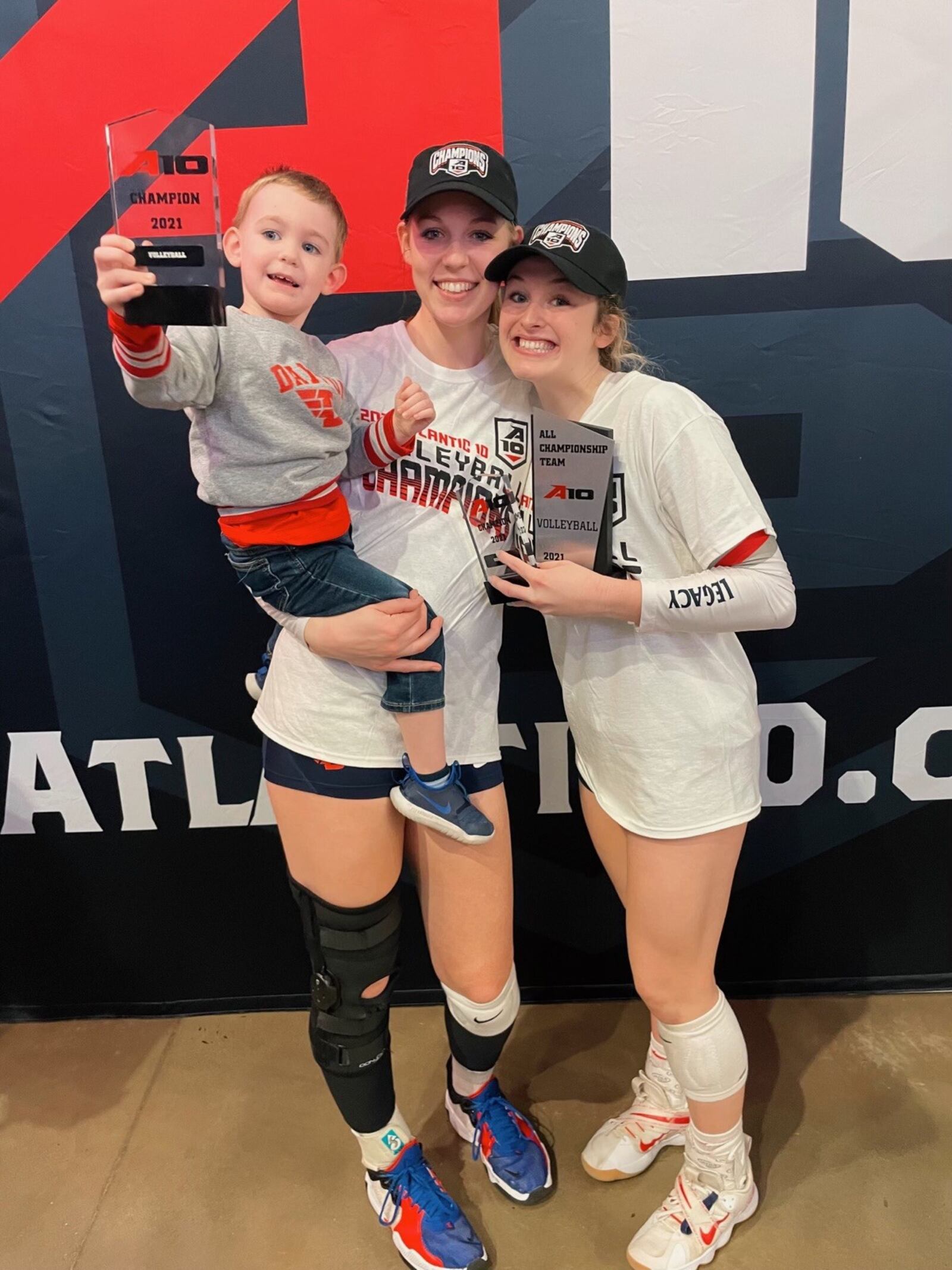 UD volleyball star Jamie Peterson and her son Carter celebrate last month with Flyers’ teammate Lexi Almodovar after Dayton won the Atlantic 10 Championship at the UPMC Cooper Fieldhouse at Duquesne University. CONTRIBUTED