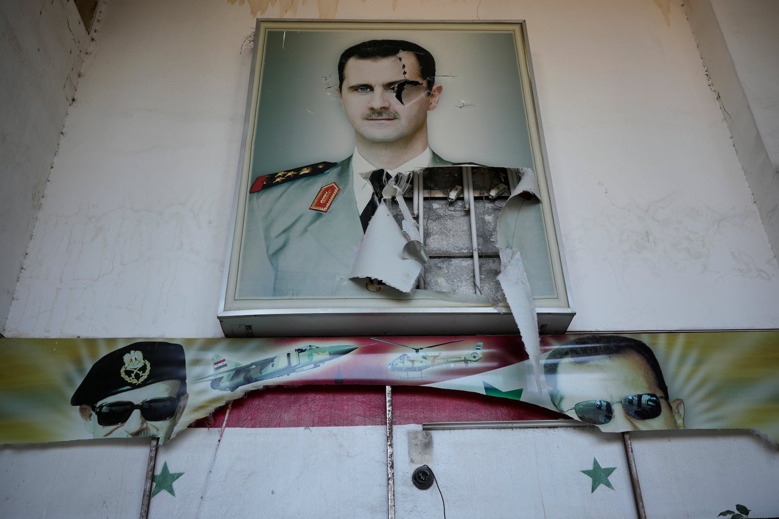 A torn posters shows the late Syrian President Hafez Assad and his son the ousted Syrian president Bashar Assad, that were set at the entrance of the notorious security detention centre called Palestine Branch, in Damascus, Syria, Saturday, Dec. 14, 2024. (AP Photo/Hussein Malla)