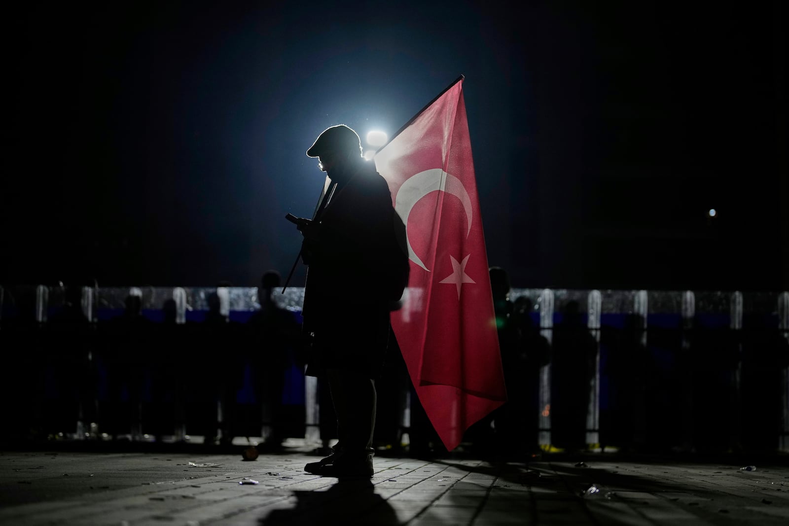 A protester holds a Turkish flag as riot police stand guard during a protest against the arrest of Istanbul's Mayor Ekrem Imamoglu, outside Caglayan courthouse, in Istanbul, Turkey, Sunday, March 23, 2025. (AP Photo/Emrah Gurel)