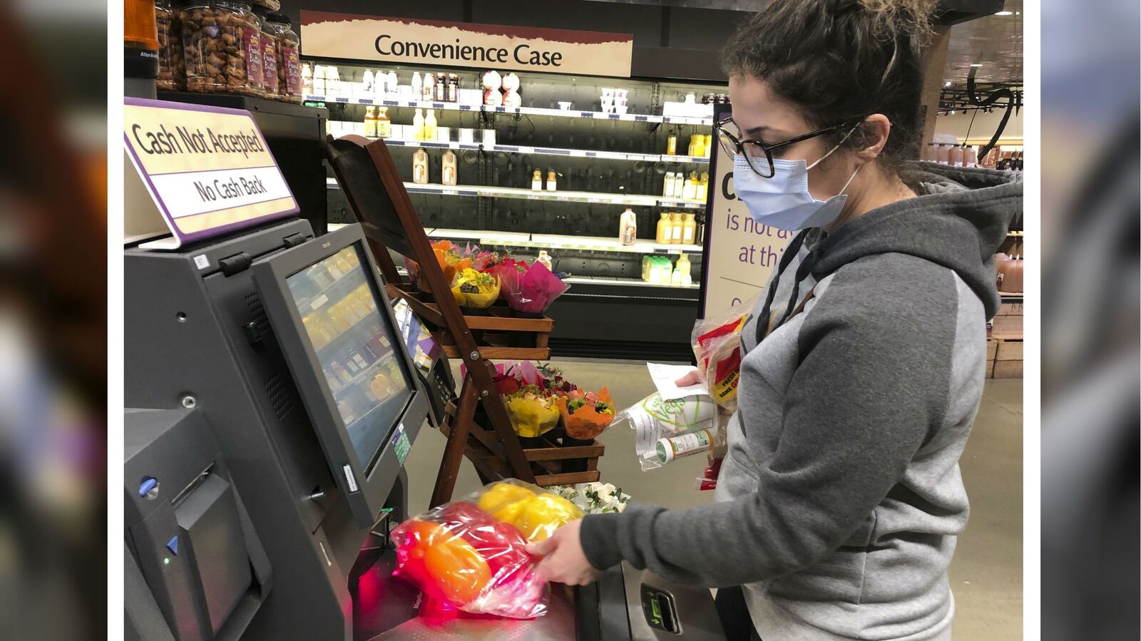 Wearing a surgical mask, Melissa Hall checks out at a Wegmans supermarket Friday, March 13, 2020, in King of Prussia, Pa.