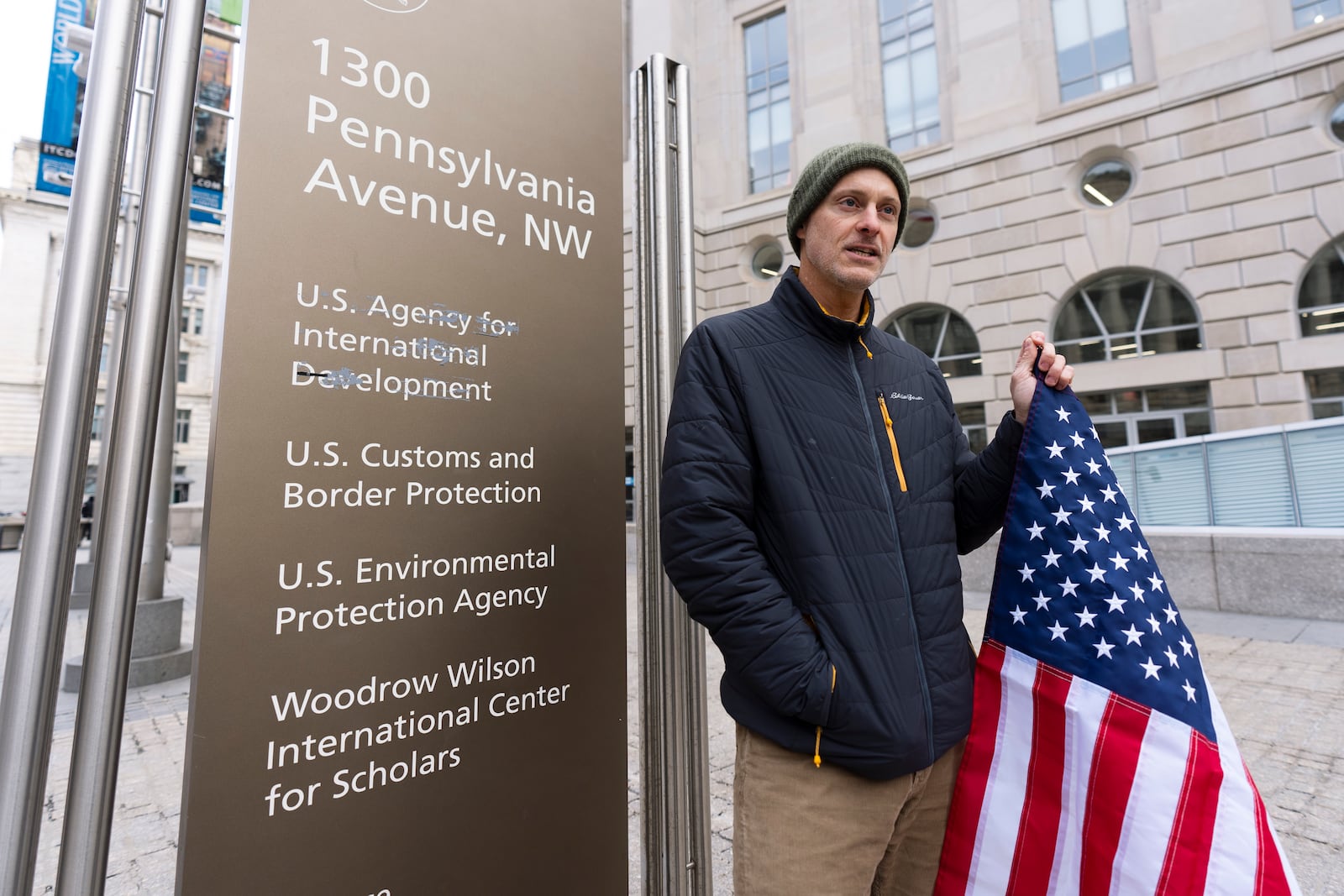 Taylor Williamson, who works for a company doing contract work for the United States Agency for International Development, or USAID, holds an American flag as he stands outside the USAID headquarters in Washington, Monday, Feb. 10, 2025. (AP Photo/Manuel Balce Ceneta)