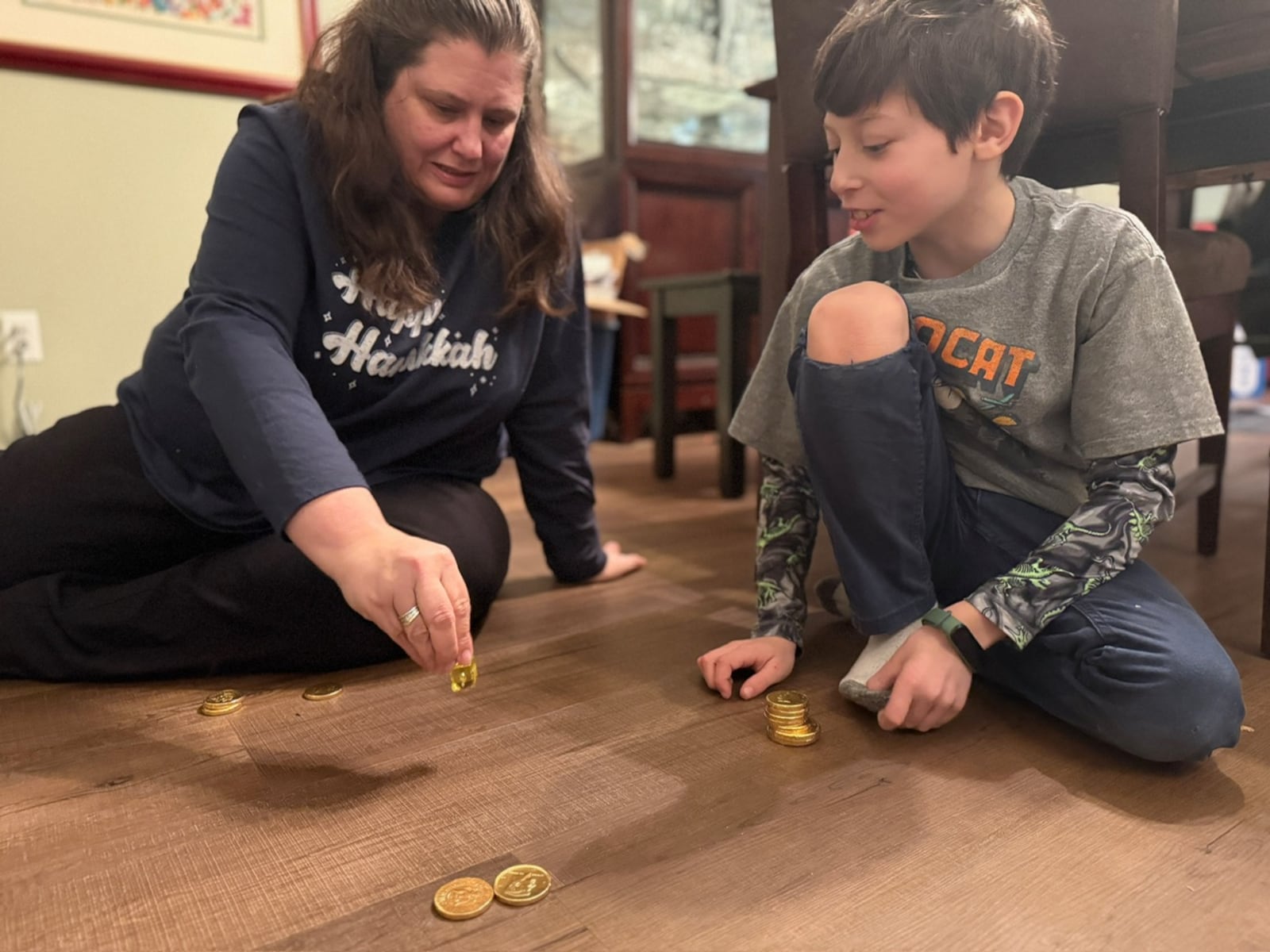 Karen Bodney-Halasz plays dreidel with her son, Ethan. The game involves a spinning top.  Chocolate coins are used as tokens.