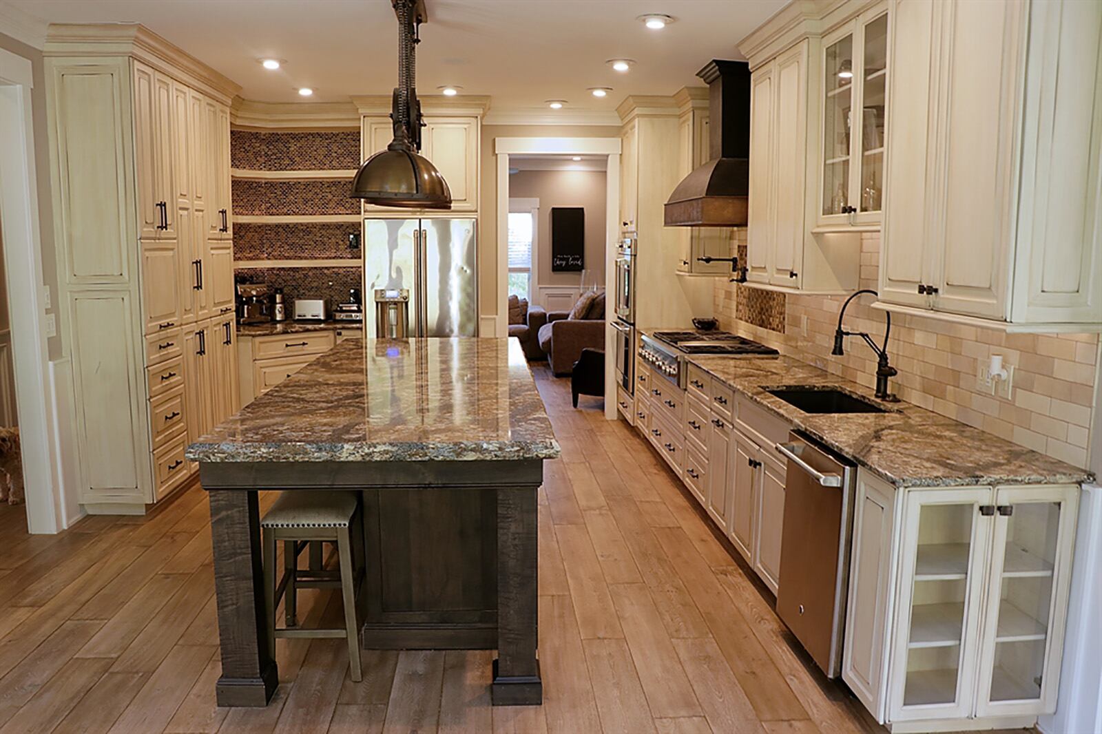 Distressed-stained white Amish-built cabinetry fills two walls in the kitchen, allowing for plenty of storage within cabinetry, drawers and lift-panel appliance garages. Tucked into one corner is a coffee station with mosaic-glass backsplash accenting multiple shelves and a granite counter. An island has a chiseled-edge granite countertop and retractable heat lamps hang above the island. CONTRIBUTED PHOTO BY KATHY TYLER