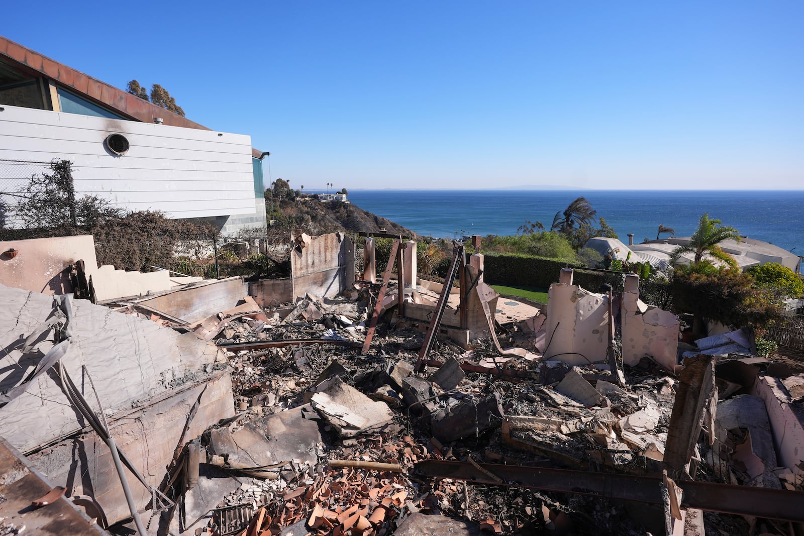 Debris from a home destroyed by the Palisades Fire is seen next to a home still standing in Malibu, Calif., Sunday, Jan. 12, 2025. (AP Photo/Mark J. Terrill)