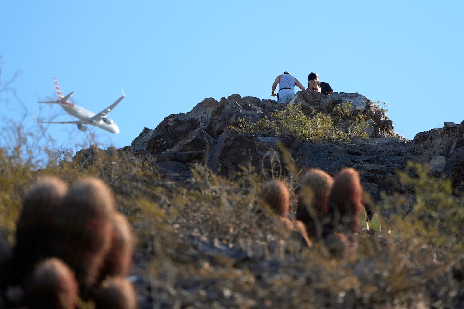 Hikers climb "A" Mountain as a passenger jet flies over Tuesday, Sept. 24, 2024, in Tempe, Ariz. (AP Photo/Ross D. Franklin)