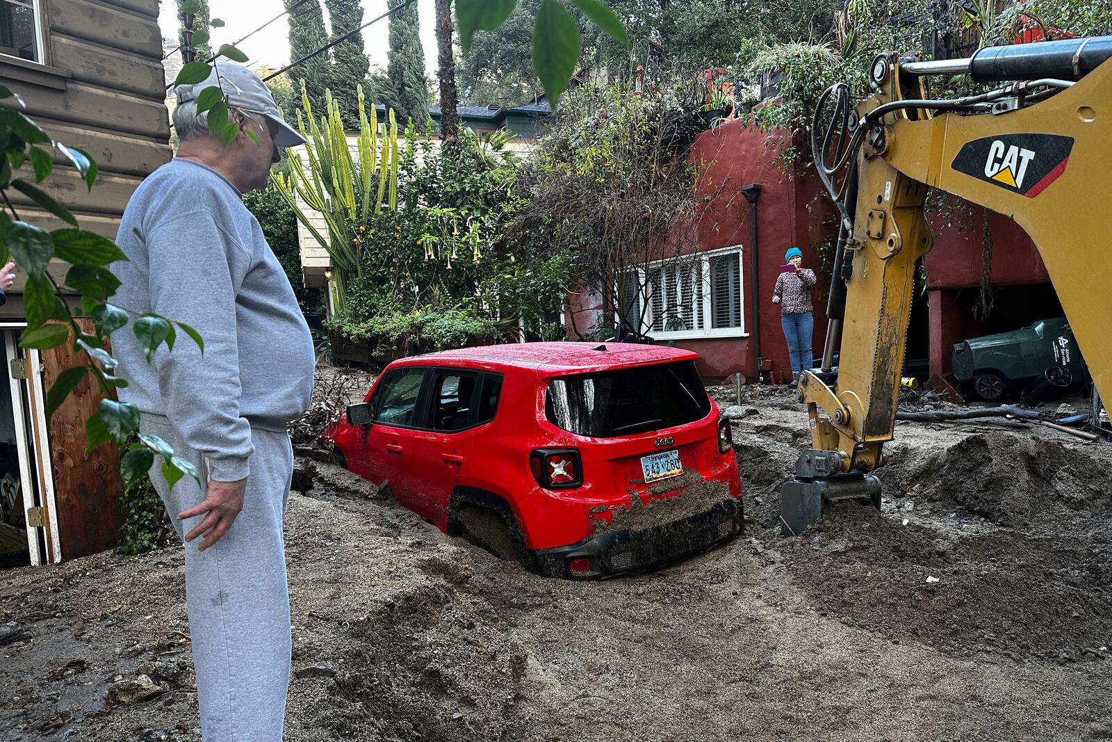 Residents watch as a vehicle is dug out of the mud after a storm Friday, Feb. 14, 2025, in Sierra Madre, Calif. (AP Photo/Eugene Garcia)