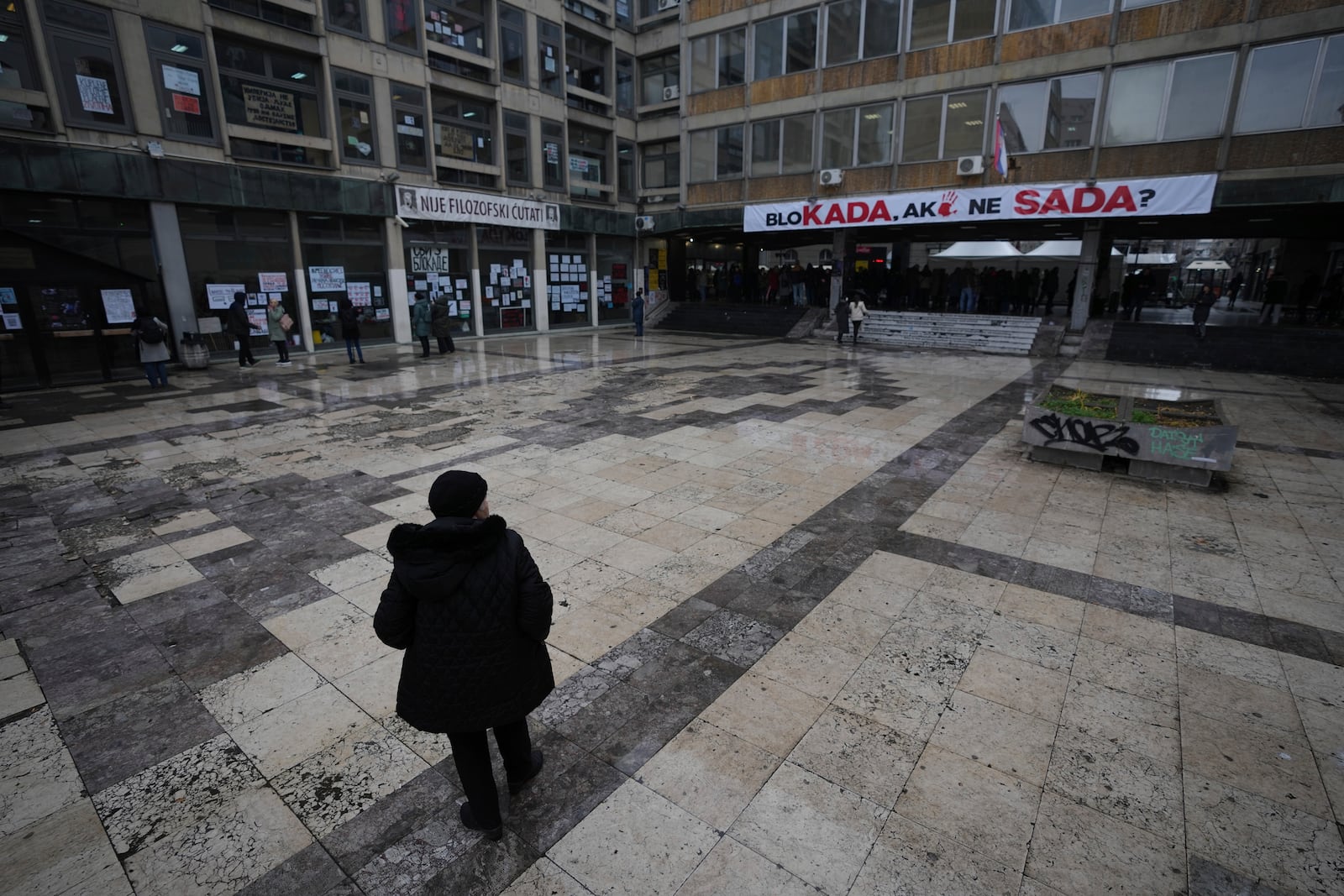 A woman stands in front of the University building where students are camping in ongoing protests that erupted after a concrete canopy fell last month and killed 15 people, in Belgrade, Serbia, Friday, Dec. 20, 2024. (AP Photo/Darko Vojinovic)