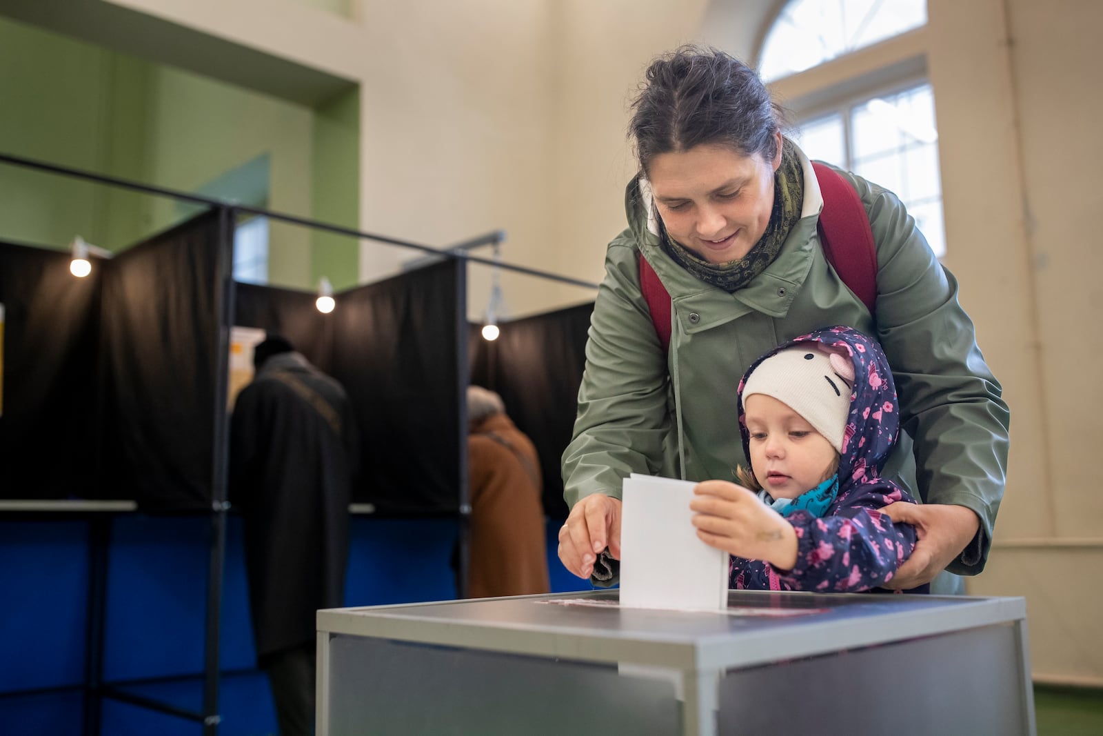 A woman with a child casts a ballot at a polling station during the first round of voting in parliamentary elections, in Vilnius, Lithuania, Sunday, Oct. 13, 2024. (AP Photo/Mindaugas Kulbis)