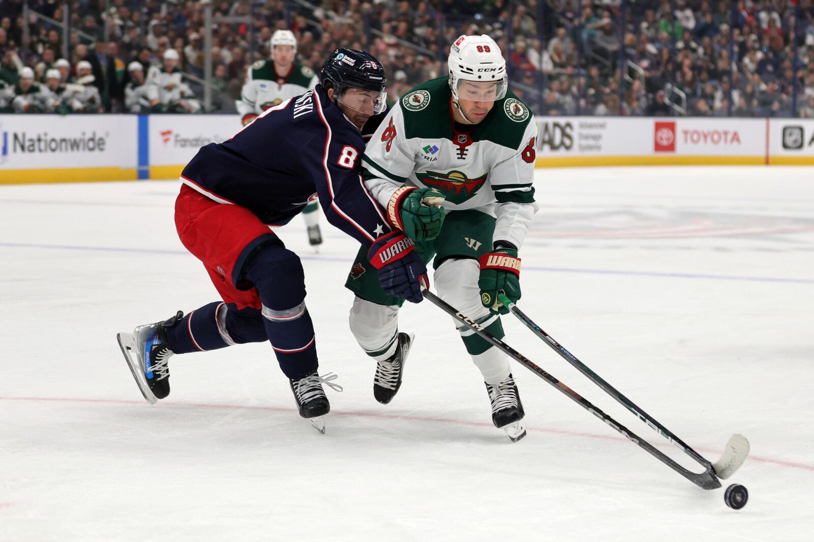 Minnesota Wild forward Frederick Gaudreau, right, reaches for the puck in front of Columbus Blue Jackets defenseman Zach Werenski during the first period of an NHL hockey game in Columbus, Ohio, Saturday, Oct. 19, 2024. (AP Photo/Paul Vernon)