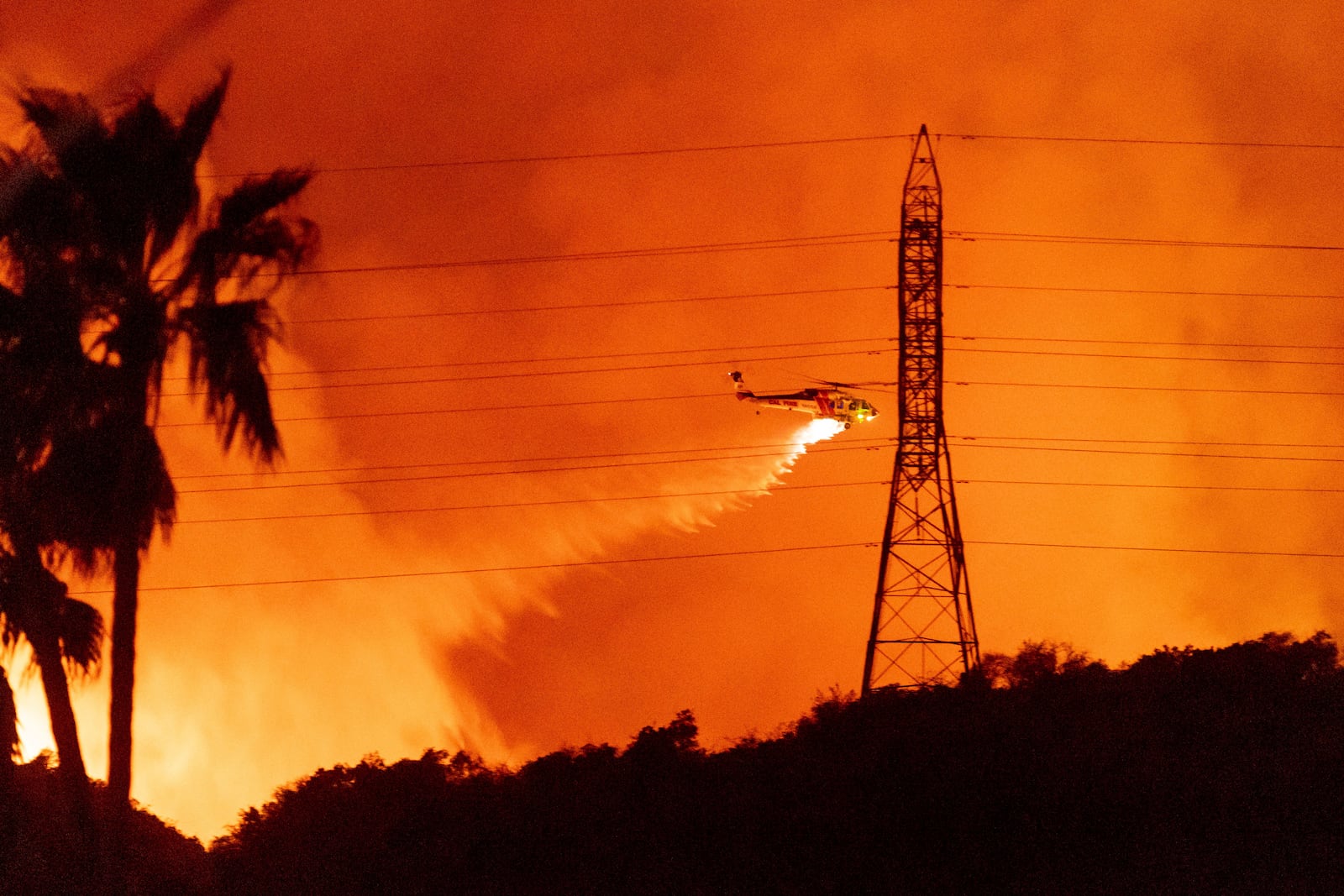 FILE - A helicopter drops water on the Palisades Fire in Mandeville Canyon, Friday, Jan. 10, 2025, in Los Angeles. (AP Photo/Ethan Swope, File)