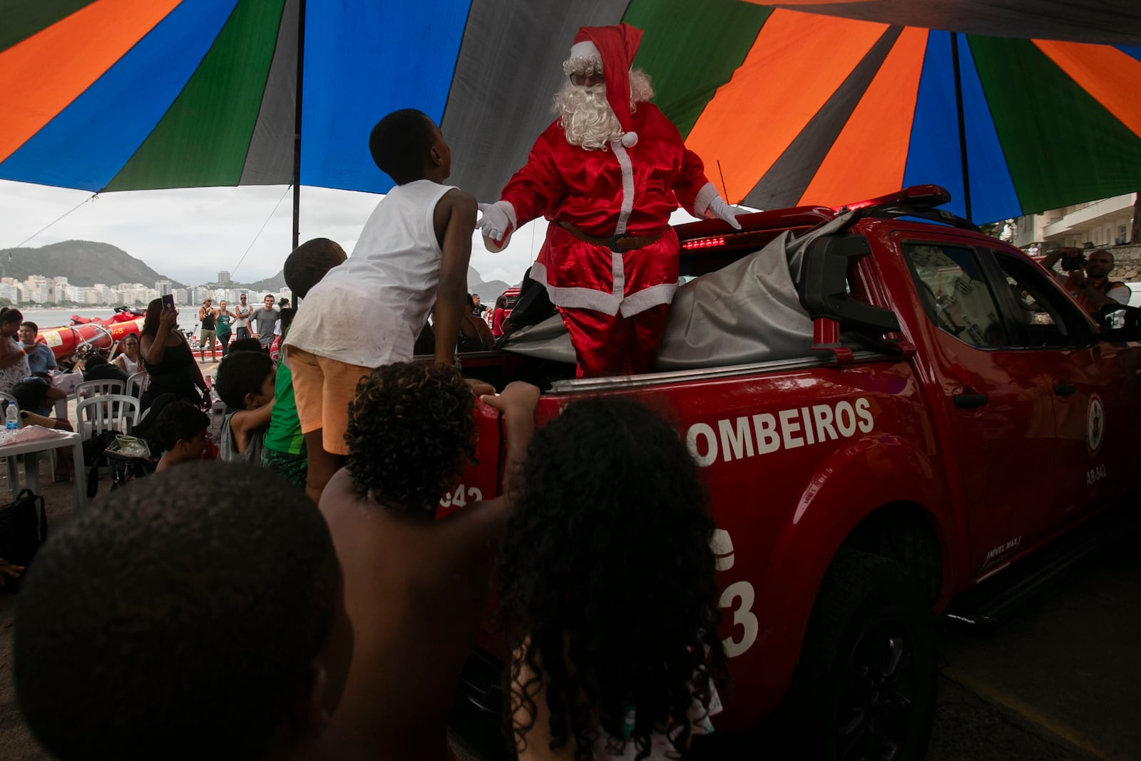 A firefighter dressed as Santa Claus entertains children on Copacabana Beach in Rio de Janeiro, Tuesday, Dec. 17, 2024. (AP Photo/Bruna Prado)