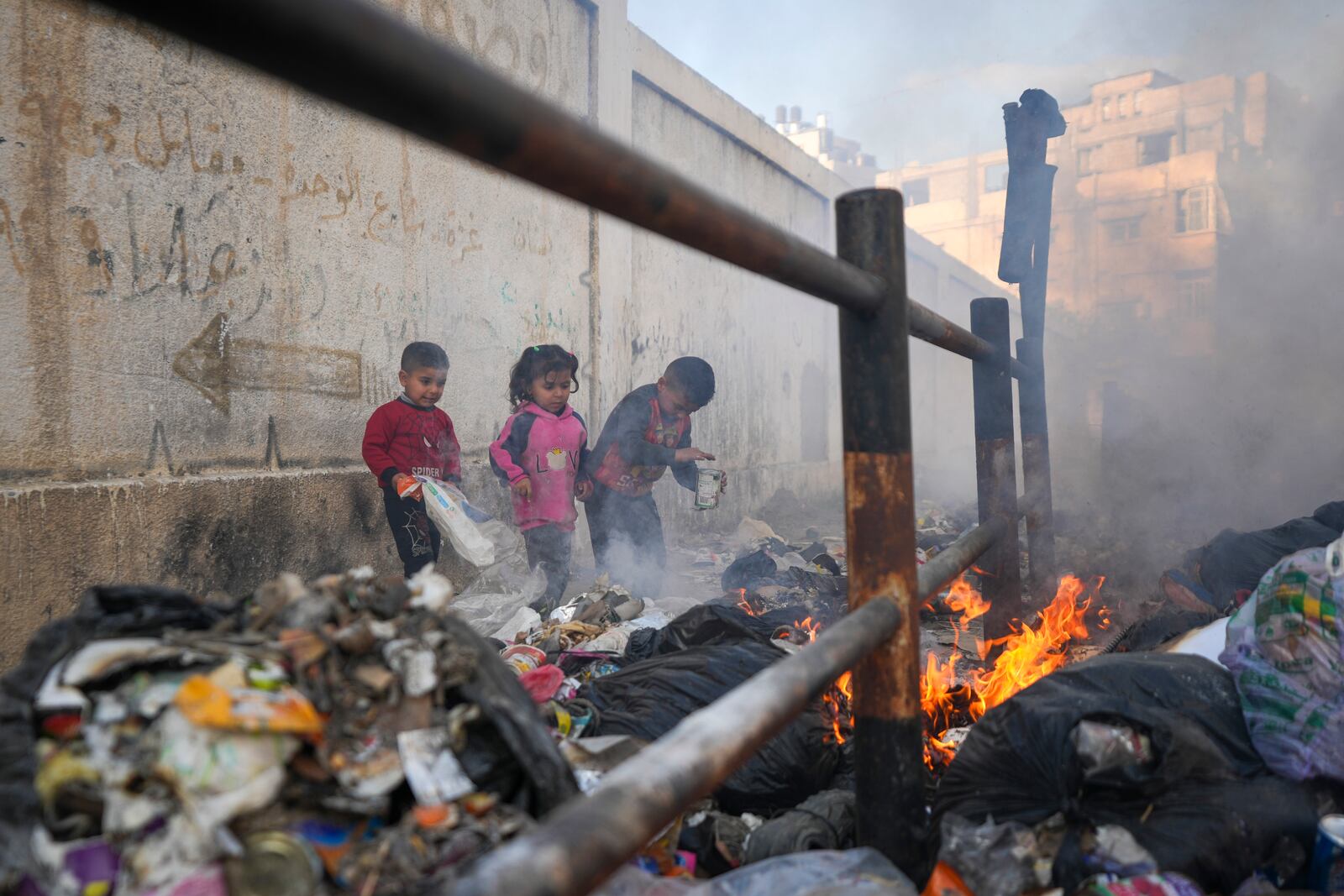 From left to right, Awad, Salma, and Mahmoud play by throwing paper onto a burning pile of garbage in the streets, as there is no refuse collection and people are disposing of their rubbish in the open, in Gaza City, Tuesday, Feb.4, 2025. (AP Photo/Abdel Kareem Hana)