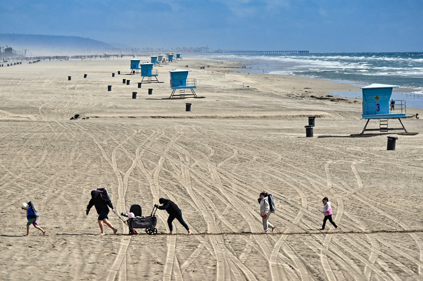 Beach goers trudge through the sand in a windy day south of the pier in Huntington Beach, Calif., Thursday, March 13, 2025, after strong storms moved through the region overnight. (Jeff Gritchen/The Orange County Register via AP)