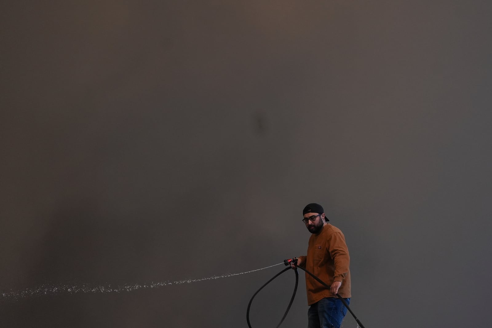 Andrew Aguilar spray water from the top of the roof at his brother's home Castaic, Calif., as a large plume of smoke caused by the Hughes Fire rises from Castaic Lake Wednesday, Jan. 22, 2025. (AP Photo/Marcio Jose Sanchez)