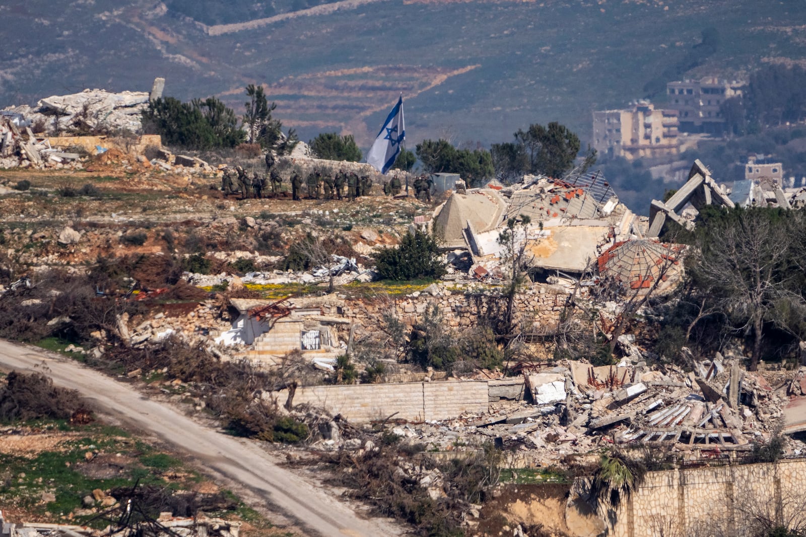 Israeli solders stand next to an Israeli flag inside a village in southern Lebanon, as seen form northern Israel, Thursday, Jan. 23, 2025. (AP Photo/Ariel Schalit)