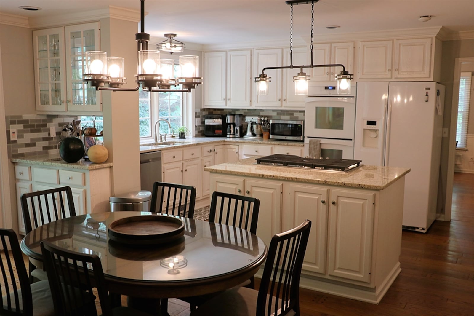 Wood flooring with peg-nail accents fills the remodeled kitchen and hearth room. White cabinetry with light granite counters wraps around to create a galley-style kitchen. 