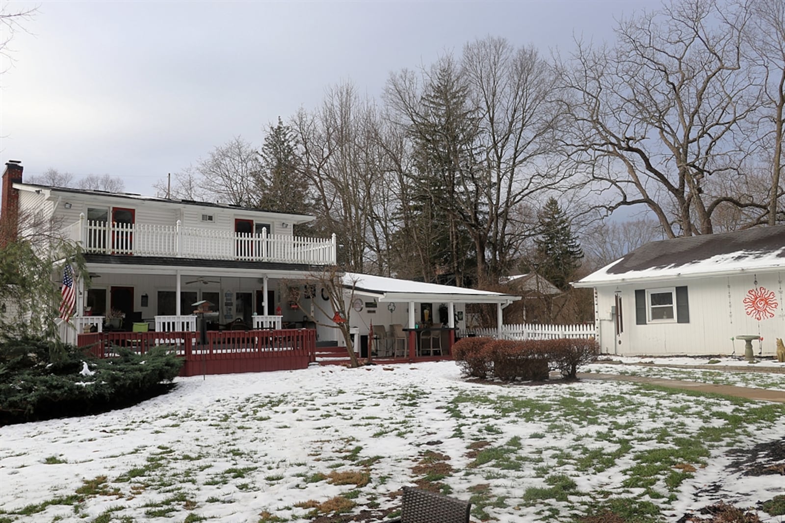 A long, paved driveway leads from the road through a picket fence to the side-entry, two-car garage and the garage entrance to the barn. 