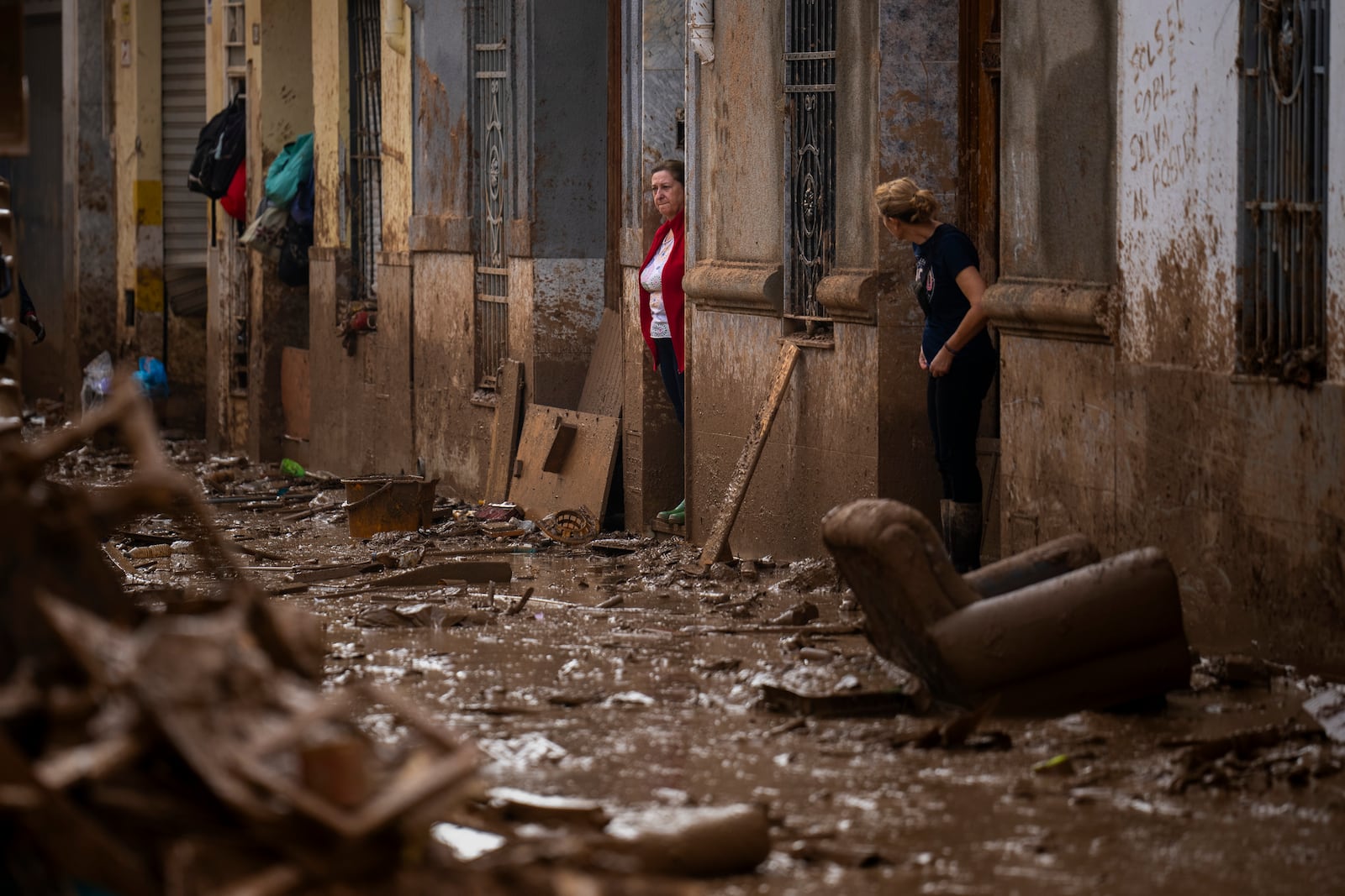 Women stand at the entrance of their houses affected by flooding in Masanasa, Valencia, Spain, Wednesday, Nov. 6, 2024. (AP Photo/Emilio Morenatti)