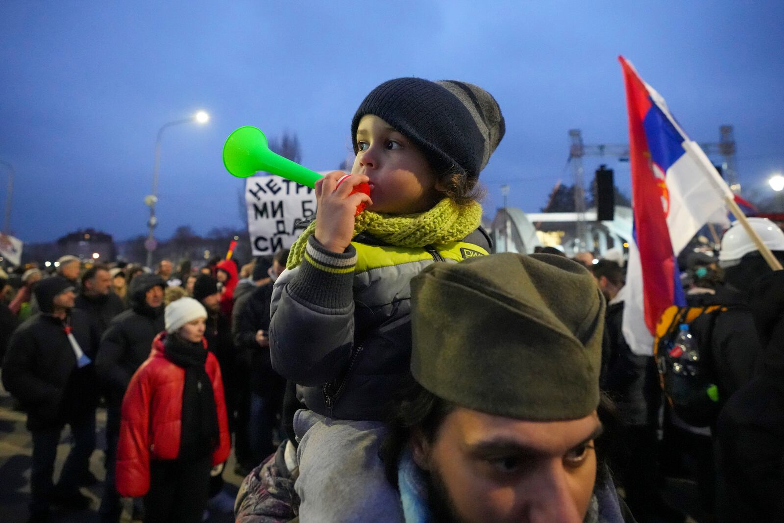 A man wearing a traditional Serbian hat with a child attends a student-led large protest and a 15-hour blockade of the streets in Serbian industrial town of Kragujevac, to protest the deaths of 15 people killed in the November collapse of a train station canopy, Saturday, Feb. 15, 2025. (AP Photo/Darko Vojinovic)