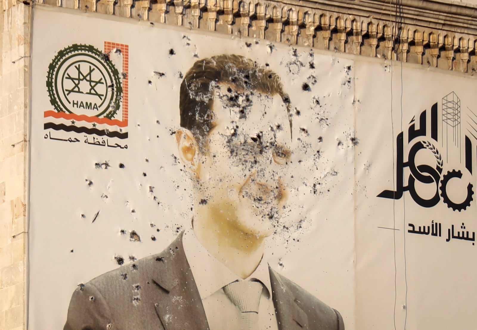 An image of Syrian President Bashar Assad, riddled with bullets, is seen on the facade of the provincial government office in the aftermath of the opposition's takeover of Hama, Syria, Friday, Dec. 6, 2024. (AP Photo/Omar Albam)