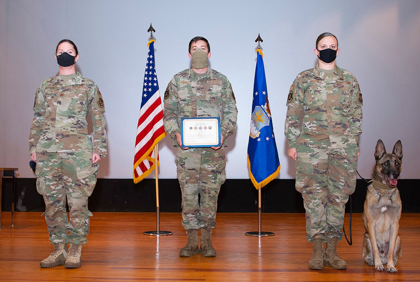 Military Working Dog Rudo and his handler, Staff Sgt. Lacey Bockman, 88th Security Forces Squadron (stage right), are presented with Rudo’s Military Working Dog Certificate of Meritorious Service by Maj. Julie Roloson (left), 88th SFS commander, during Rudo’s retirement ceremony Nov. 16 in the theater at Wright-Patterson Air Force Base. U.S. AIR FORCE PHOTO/R.J. ORIEZ