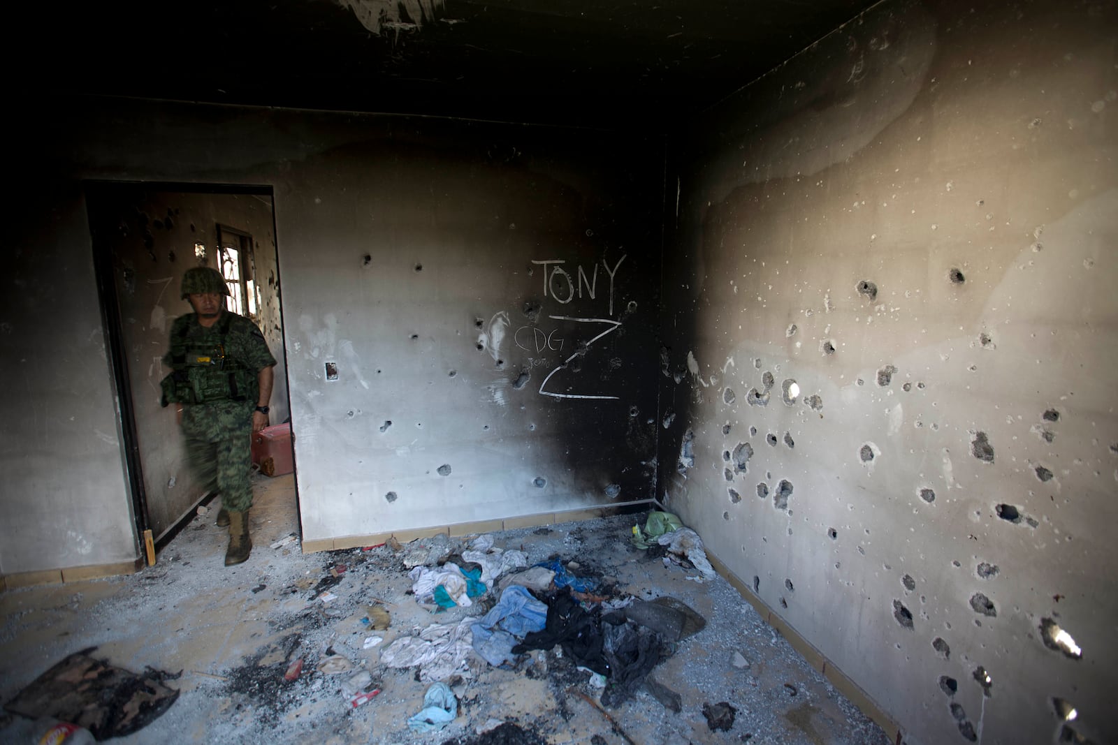 FILE - A soldier enters a bullet-riddled home covered by the initials of the Gulf Cartel (CDG) and Zetas (Z) in Ciudad Victoria, Tamaulipas state, Mexico, Sept. 6, 2014. (AP Photo/Eduardo Verdugo, File)