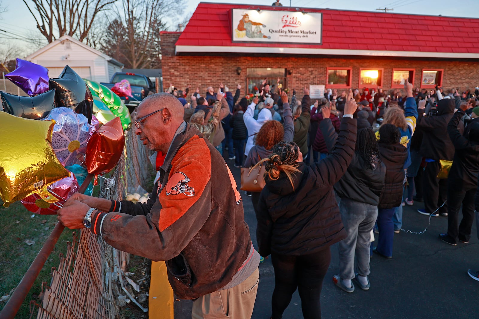 Mario Evans ties a balloon to a fence next to Gill's Quality Meat Market Monday, Jan. 9, 2023 during a candle light vigil for local business owner Thomas Gill, who was shot and killed last Thursday while driving his SUV. BILL LACKEY/STAFF