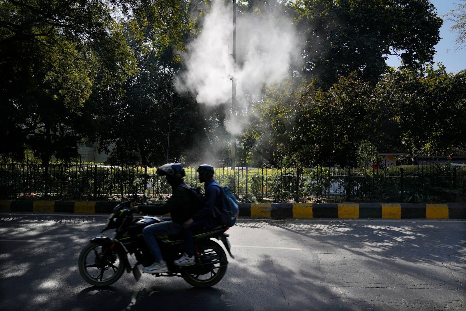 FILE - A motorcyclist drives past sprinklers that spray water in hopes of settling dust and calming air pollution in New Delhi, Feb. 12, 2025. (AP Photo/Manish Swarup, File)