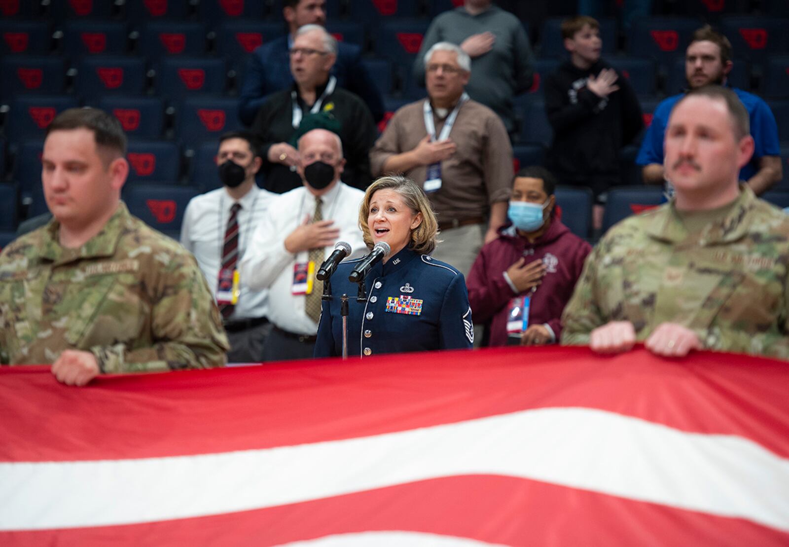 Master Sgt. Christin Foley, Air Force Band of Flight, sings the national anthem March 15 during the opening ceremony of the first game in the NCAA men’s basketball tournament between Texas Southern and Texas A&M-Corpus Christi at University of Dayton Arena as Airmen from Wright-Patterson Air Force Base display a large American flag. U.S. AIR FORCE PHOTO/R.J. ORIEZ