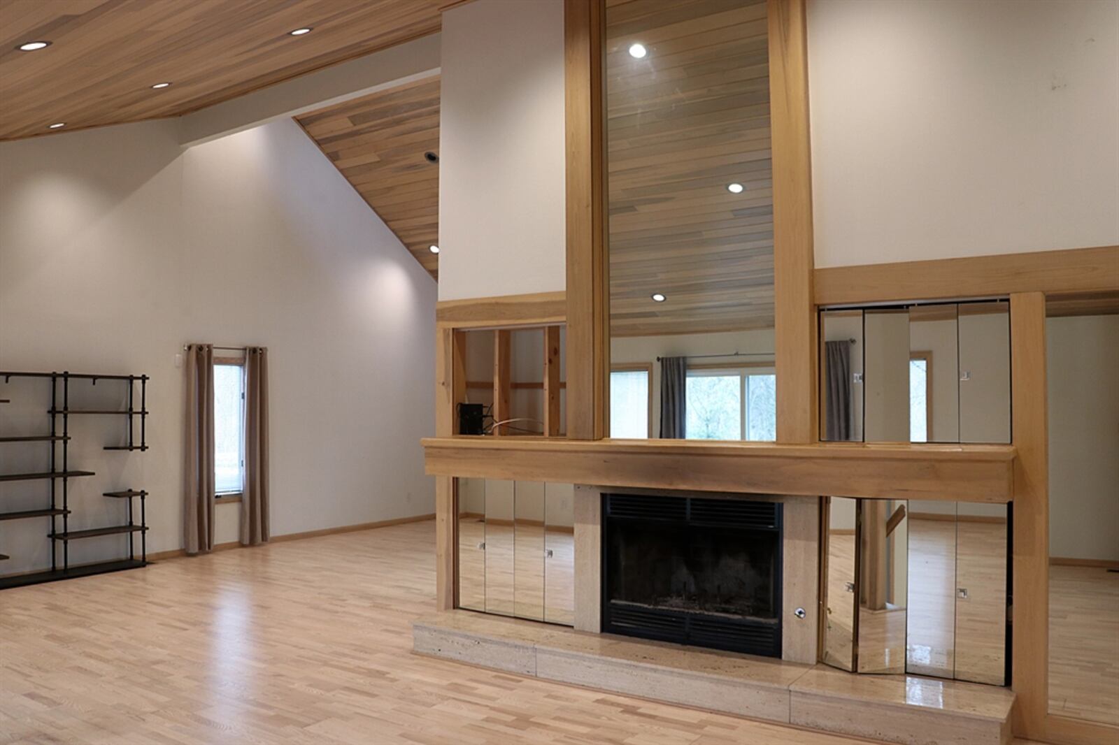 Hardwood flooring with matching wood-plank ceiling treatment highlights the combined formal areas. The vaulted ceiling has plenty of canister lights and peaks above the wood-burning fireplace. The wood mantel is surrounded by mirrored storage nooks and the raised hearth matches the travertine tile.