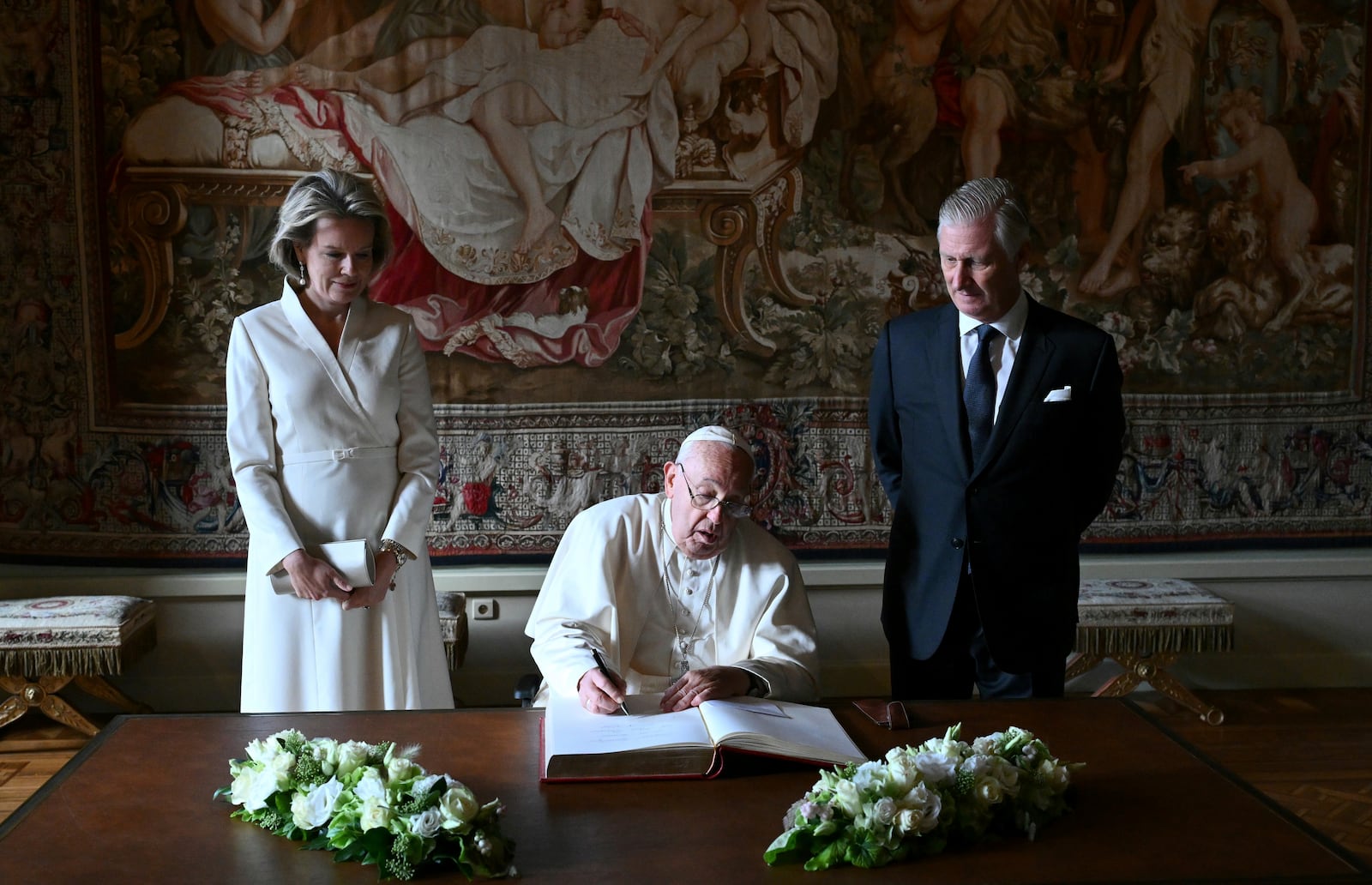 Pope Francis, center, signs the book of honor during his visit to King Philippe of Belgium, right, and Queen Mathilde at the Castle of Laeken, Belgium, Friday, Sept. 26, 2024, on the second day of a four-day apostolic journey to Luxembourg and Belgium. (Alberto Pizzoli/pool photo via AP)