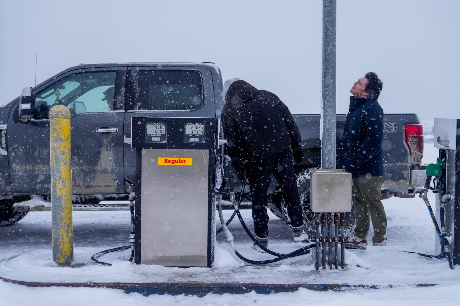 Edwin Solomon, 18, right, stands in the wind and snow while filling up a truck with regular gas at a price of $7.50 a gallon in Kaktovik, Alaska, Wednesday, Oct. 16, 2024. (AP Photo/Lindsey Wasson)