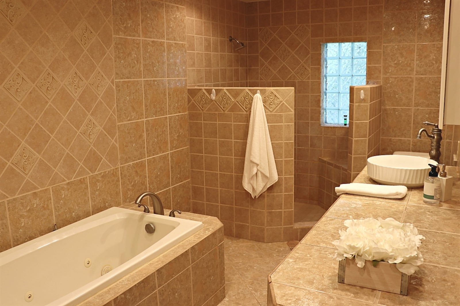 The primary bathroom is surrounded by ornate, neutral ceramic tile from the floor to the ceiling. 