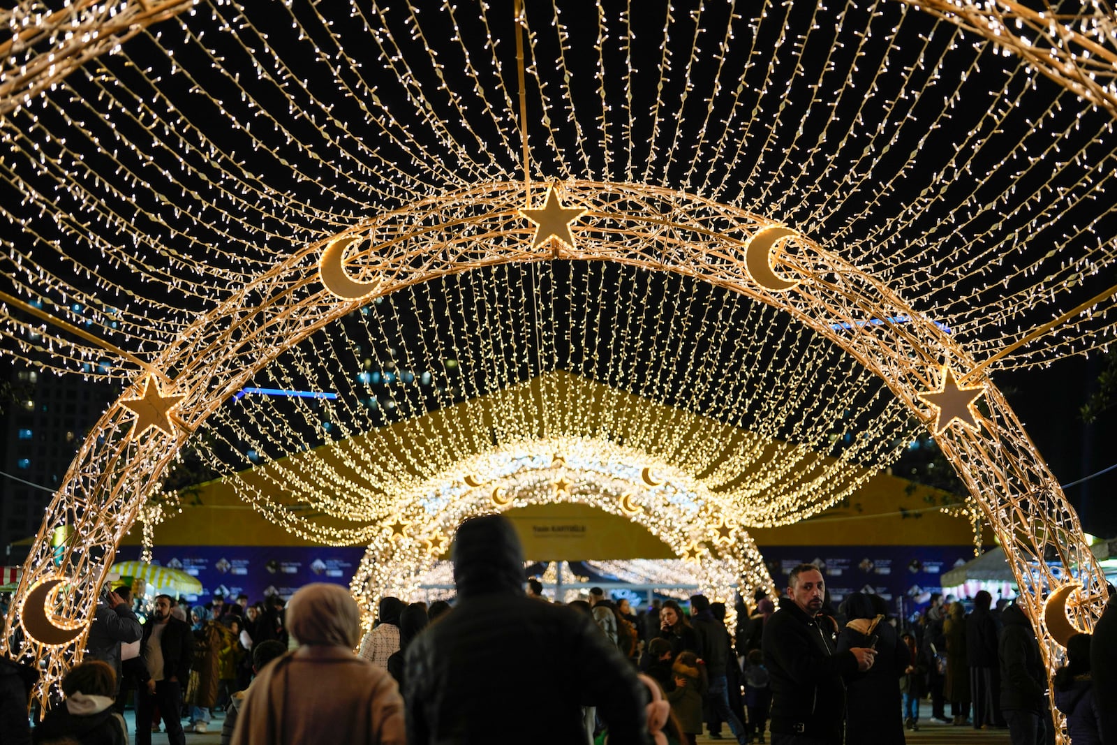 People walk under lighting decorations in a square on the first day of the Muslim holy month of Ramadan in Istanbul, Turkey, Saturday, March 1, 2025. (AP Photo/Khalil Hamra)