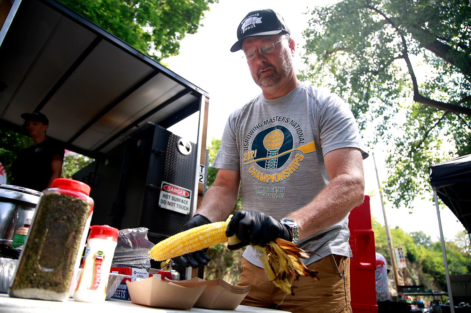 Todd Corban, from Wholly Smokes BBQ, covers an ear of roasted corn with butter for a customer Saturday, August 17, 2024 at the 10th annual Springfield Rotary Gourmet Food Truck Competition in Veterans Park. BILL LACKEY/STAFF