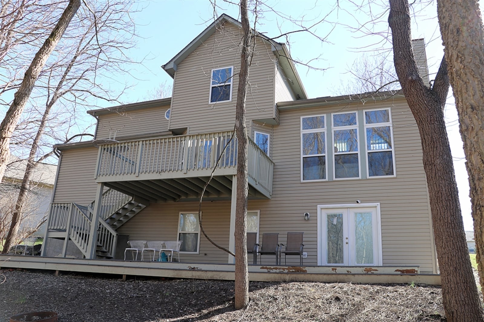 A wooden deck porch extends across the back of the house and wooden steps ascend to the balcony deck. The yard has a fire pit and storage shed. 