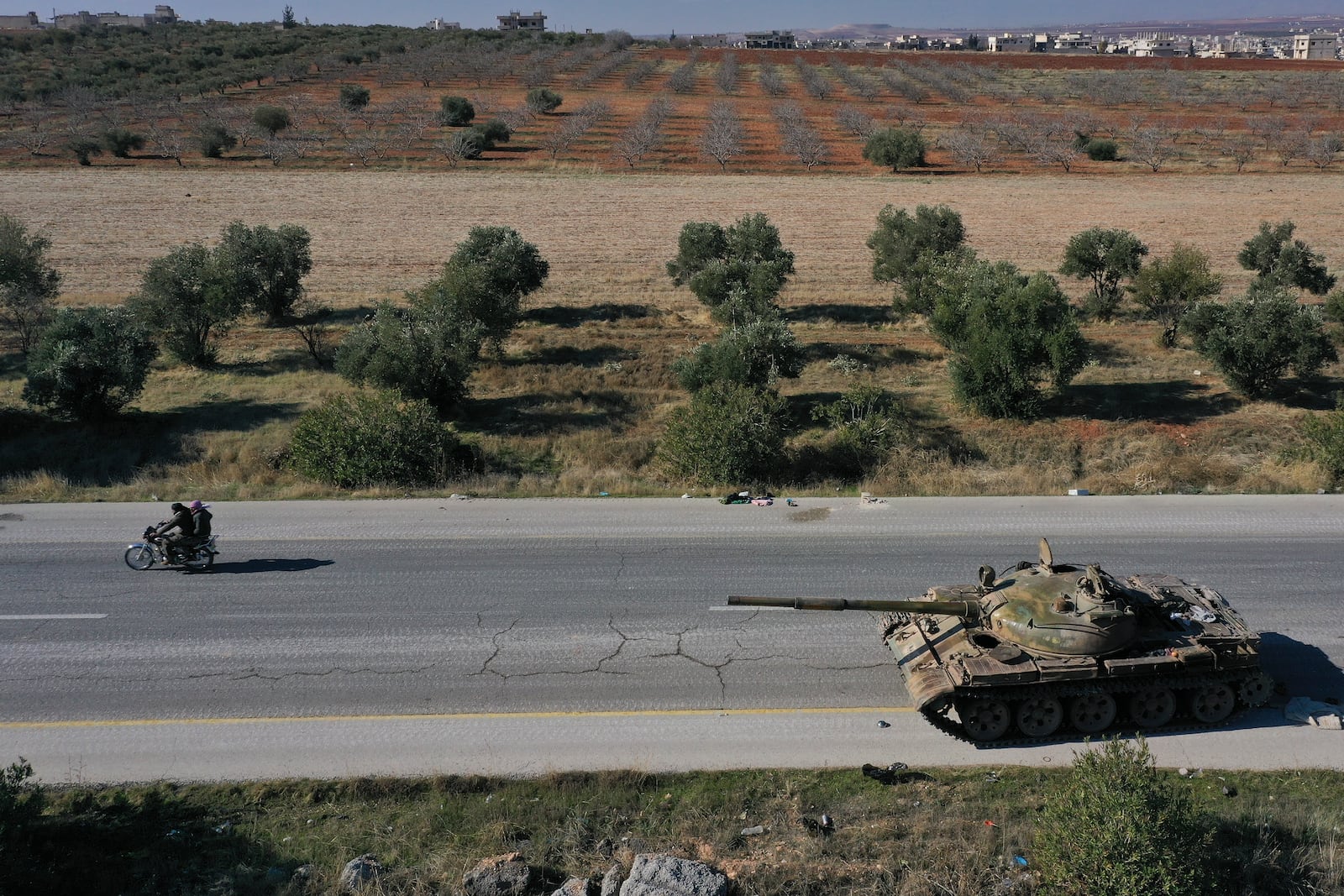 Syrian opposition fighters ride on a motorcycle by an abandoned Syrian army armoured vehicle on a road in the outskirts of in Khan Sheikhoun, southwest of Aleppo, Sunday, Dec. 1, 2024. Syrian opposition insurgency launched a campaign on Wednesday with a two-pronged attack on Aleppo and the countryside around Idlib.(AP Photo/Ghaith Alsayed)