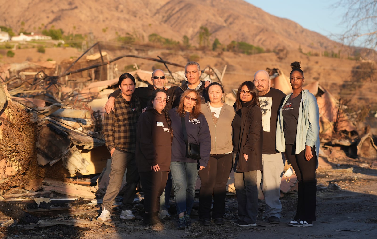 Terraces at Park Marino assisted living facility staff members, back row from left, Juan Pablo Sandoval, Sam Baum and Diversified Healthcare Services President/CEO Adam Khalifa, and front row from left, Sharon Gallego, Maria Quizon, Katherine Castro, Maggie Jay, Edgardo Exia Jr. and Lashawna Thompson pose together amidst the charred remains of the facility on Monday, Jan. 13, 2025, in Pasadena, Calif. (AP Photo/Chris Pizzello)