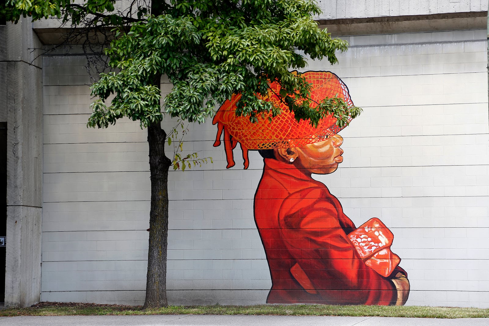 A regal woman, holding a clutch under her arm and wearing a veiled hat, is painted in tones of orange and red on the side of the transportation center parking garage on Fifth Street near the entrance to the Oregon District. She looms large against the concrete back drop while discretely painted near her is a red cardinal perched on a metal standpipe connector. LISA POWELL / STAFF