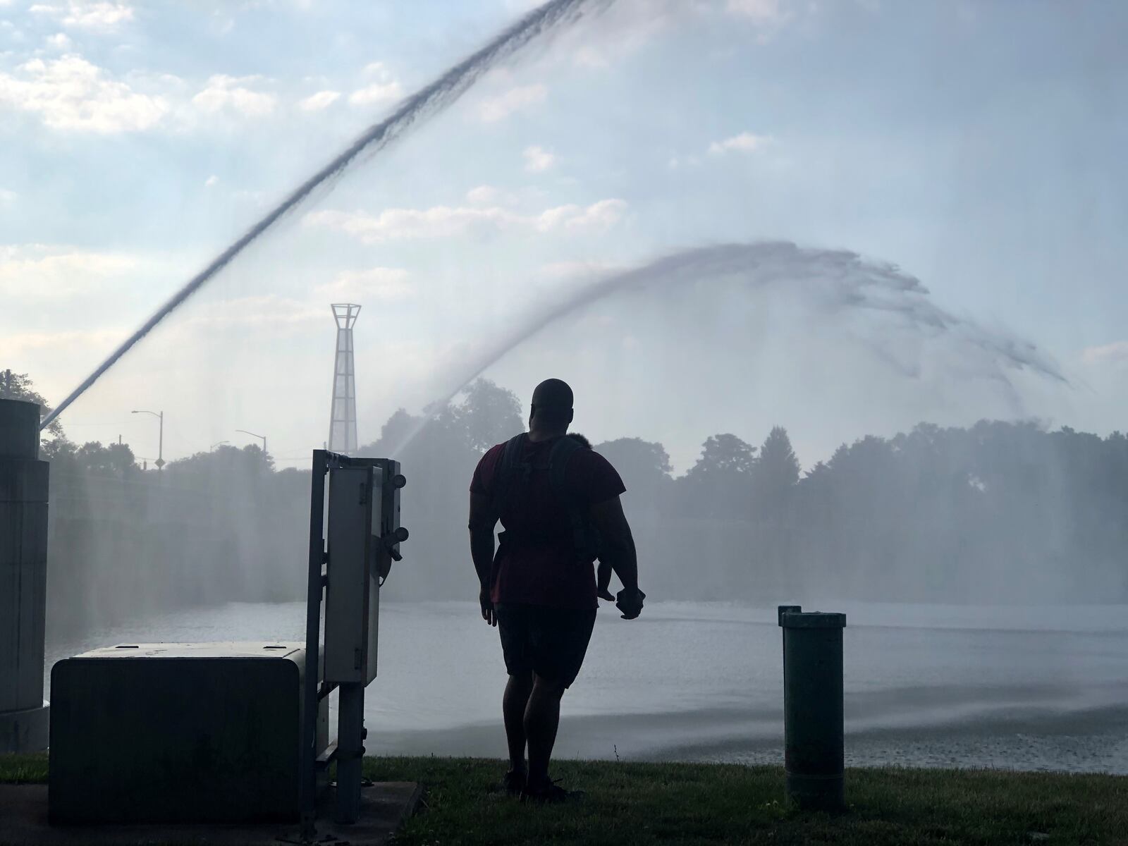 A man with a baby in a carrier watches the fountains in the river at RiverScape in the summer of 2020. CORNELIUS FROLIK / STAFF