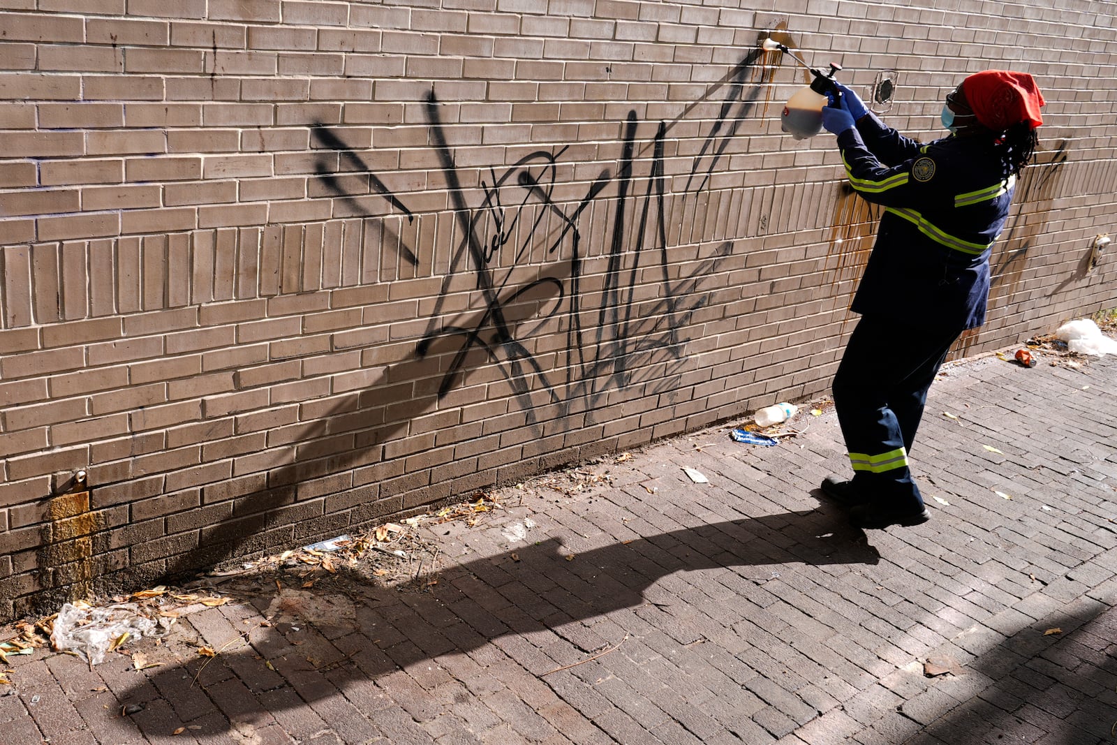 Queen Jones sprays on a chemical to remove graffiti in a neighborhood of Washington, Tuesday, Aug. 20, 2024. (AP Photo/Susan Walsh)