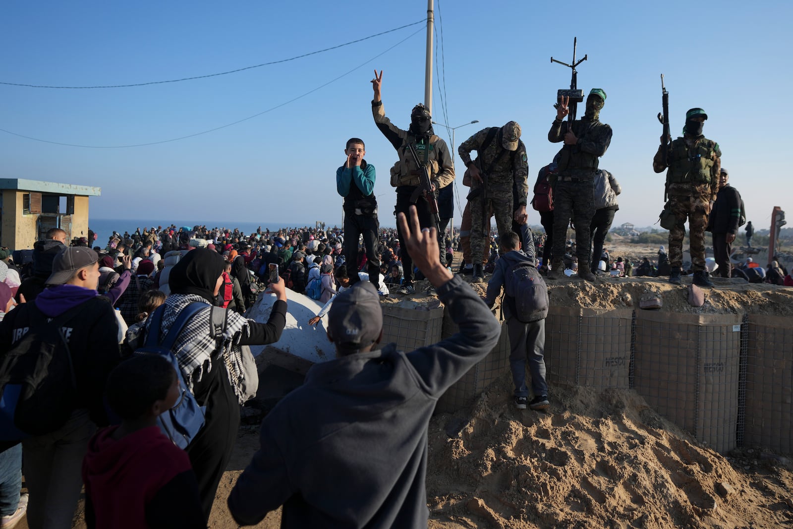 Hamas fighters flash the victory sign as displaced Palestinians return to their homes in the northern Gaza Strip, following Israel's decision to allow thousands of them to go back for the first time since the early weeks of the 15-month war with Hamas, Monday, Jan. 27, 2025. (AP Photo/Abdel Kareem Hana)