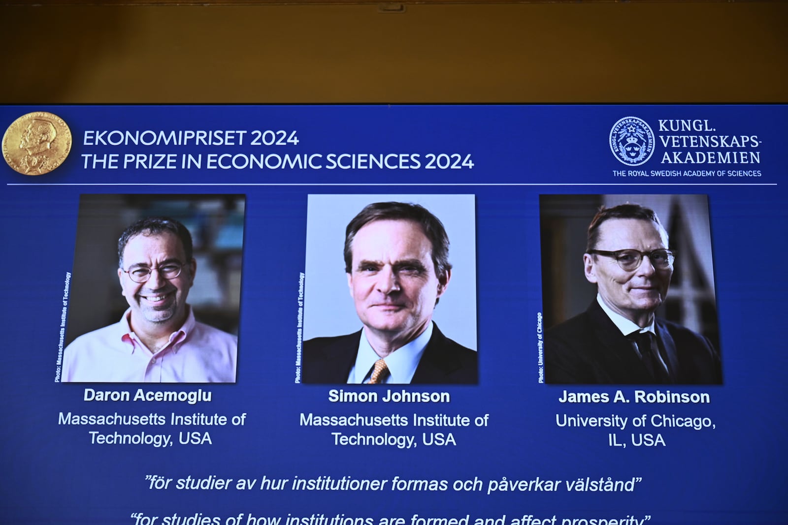 The Nobel memorial prize in economics awarded to Daron Acemoglu, Simon Johnson and James A Robinson, seen on screen, during a press meeting at the Royal Swedish Academy of Sciences in Stockholm, Sweden, Monday Oct. 14, 2024. (Christine Olsson/TT News Agency via AP)